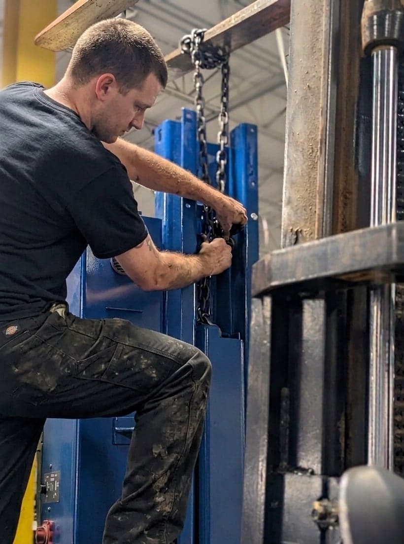 Technician servicing a two-post lift column in the bay
